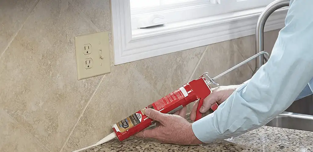 Handyman applying caulk along a kitchen backsplash and countertop seam in Houston, TX