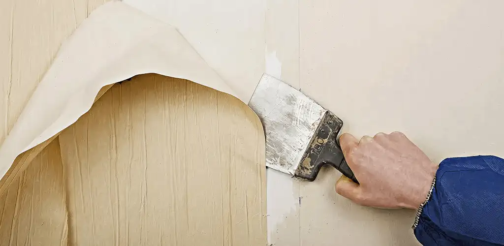 Handyman removing wallpaper with a scraper for wall preparation in Houston, TX