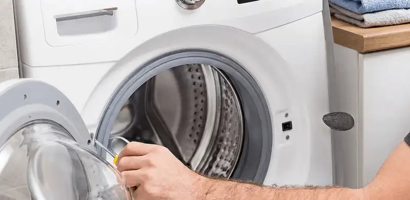 Handyman repairing a front-load washing machine and inspecting the drum in Houston, TX